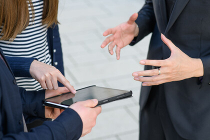 Drei Personen stehen um ein Tablet und gestikulieren mit den Händen.