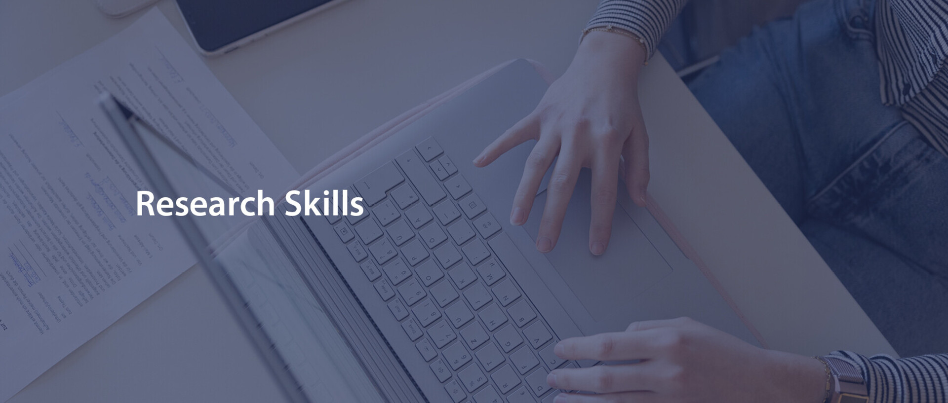 Eine Person, deren Hände im Bild sind, schreibt am Laptop. Über das Bild ist "Research Skills" ist in weißer Schrift mit blauem Hintergrund gelegt.