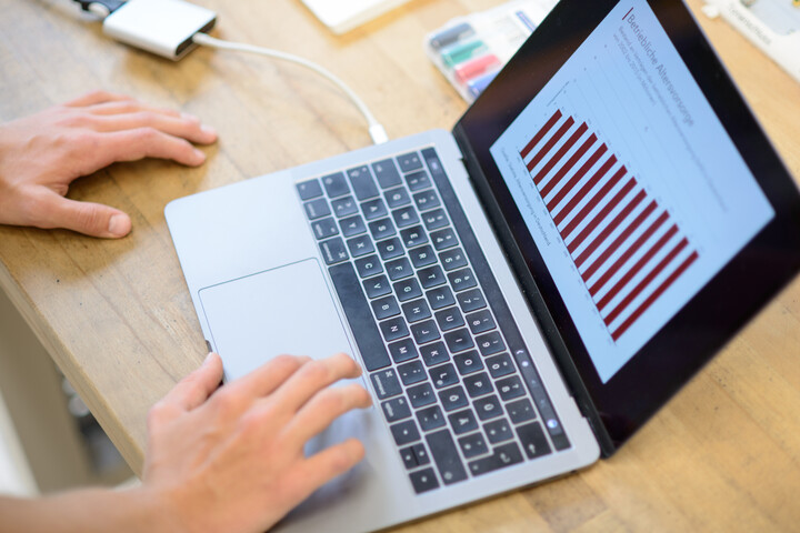 Hande schreiben an einem Laptop. Auf dem Monitor ist ein Diagramm.